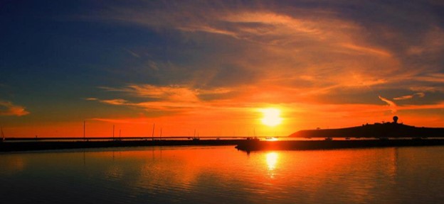 Sunrise or sunset by a quiet jetty with a hillside in the distance